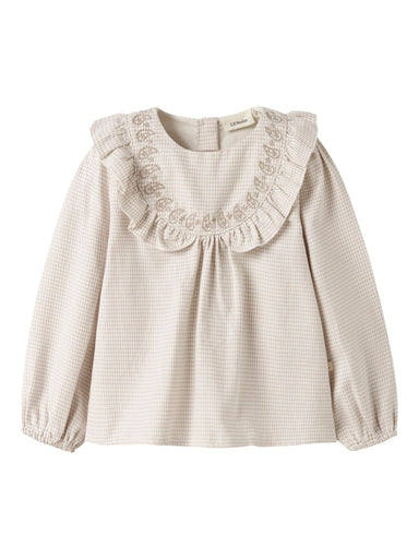 "Barn iført Lil’ Atelier NMFFOLEY LS Loose Shirt – Coconut Milk, langærmet skjorte med bedstefar-udskæring, broderi og flæsedetaljer, lavet af 100% økologisk bomuld, set forfra."