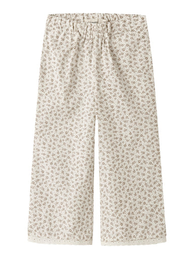 "Barn iført Lil’ Atelier NMFFJOLA Wide Ancle Pant – Coconut Milk, wide leg fit, justerbar talje og blondedetaljer, lavet af 100% økologisk bomuld, set forfra."